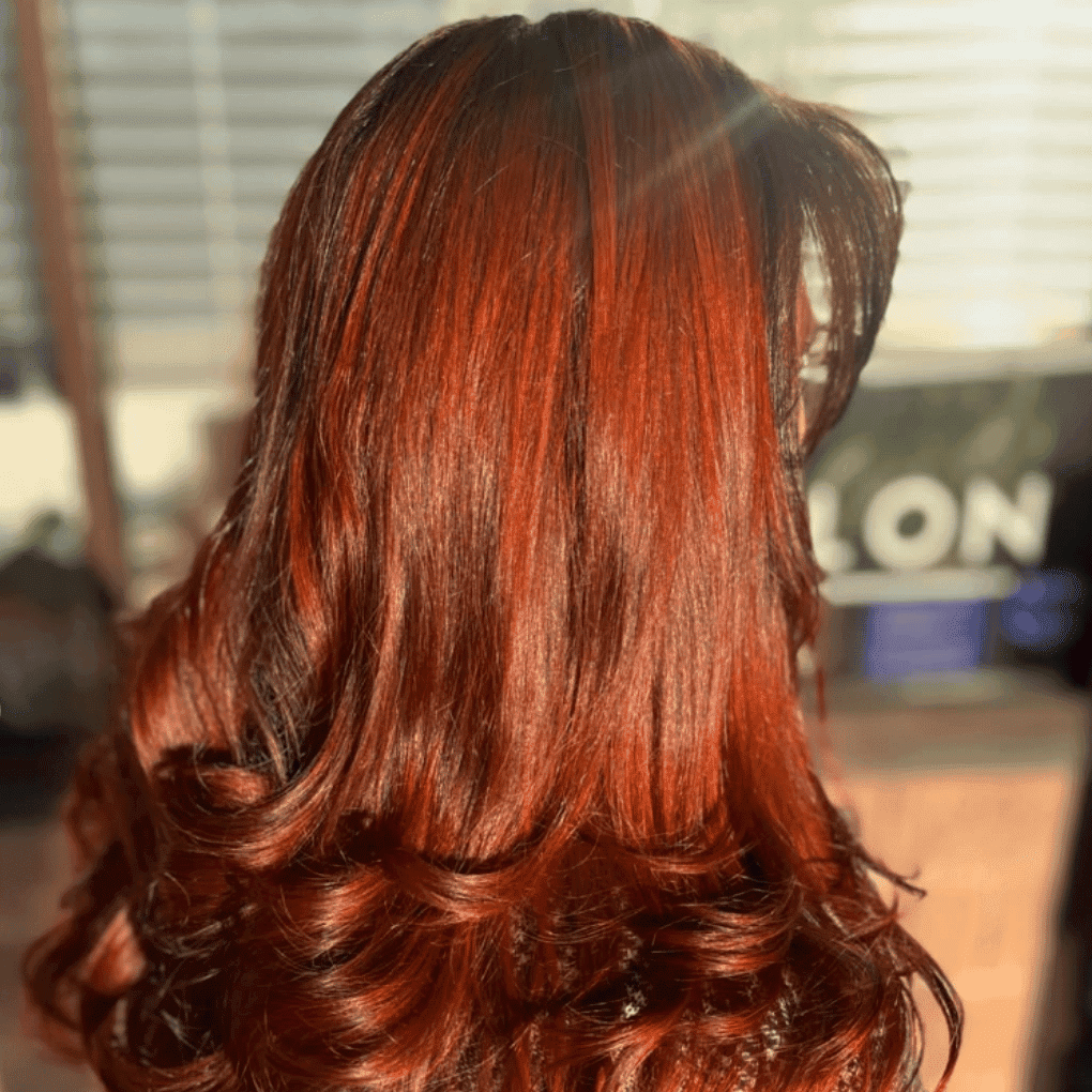 Rich red hair with curls, glistening under sunlight in a salon setting.