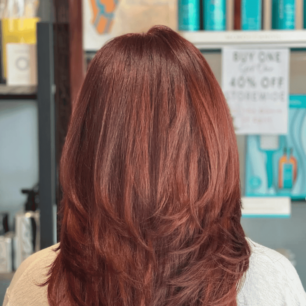 Red hair styled in layers, with beauty products on shelf in background.