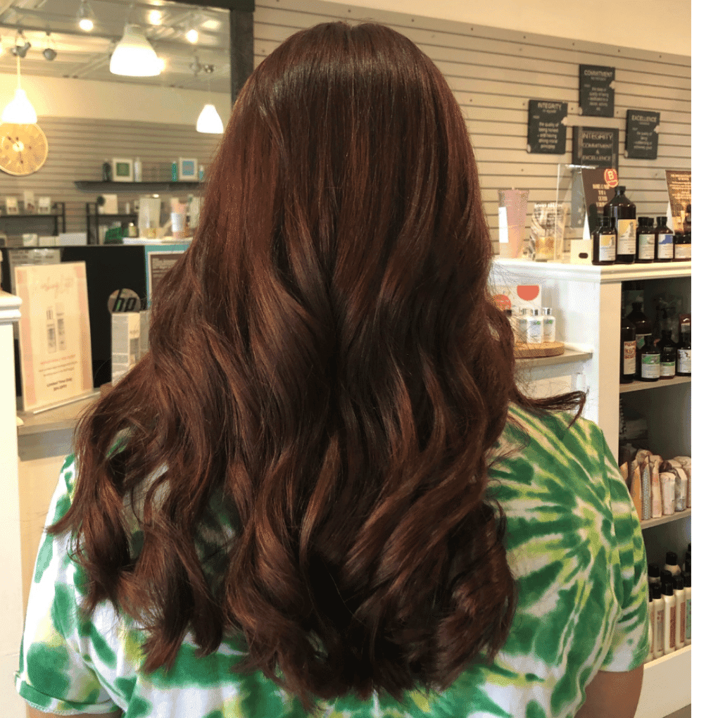 Brown wavy hair at a salon, person wearing a green tie-dye shirt, shelves in the background.