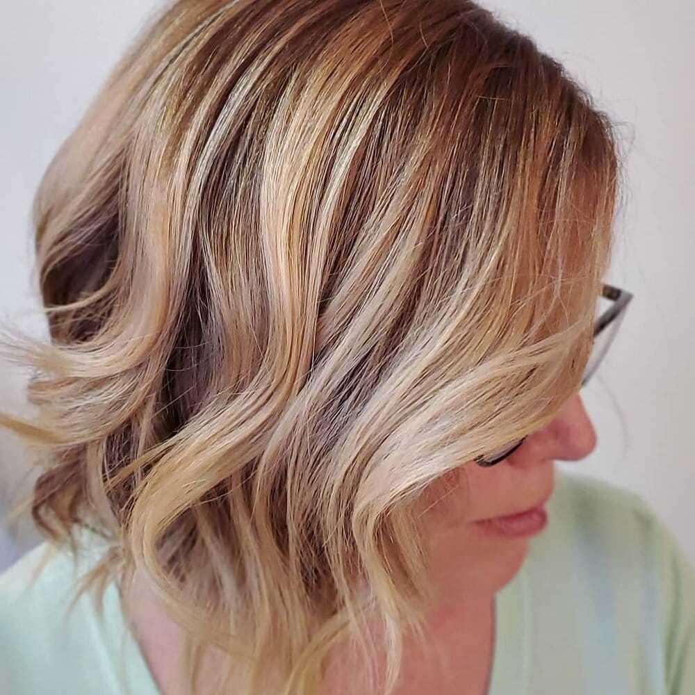 Woman with wavy, shoulder-length blonde hair and glasses, side profile view.