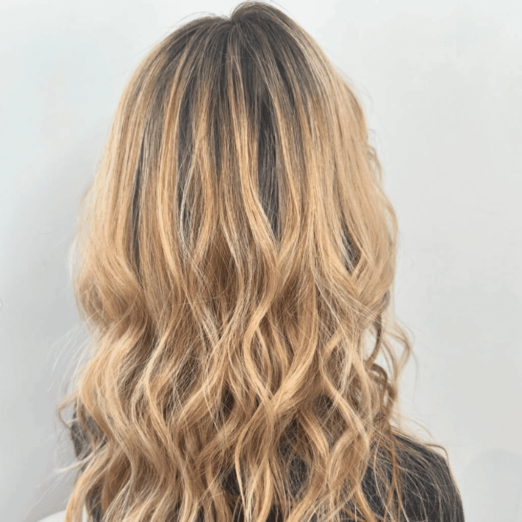 Blonde wavy hair with dark roots, styled in cascading curls from the back view.